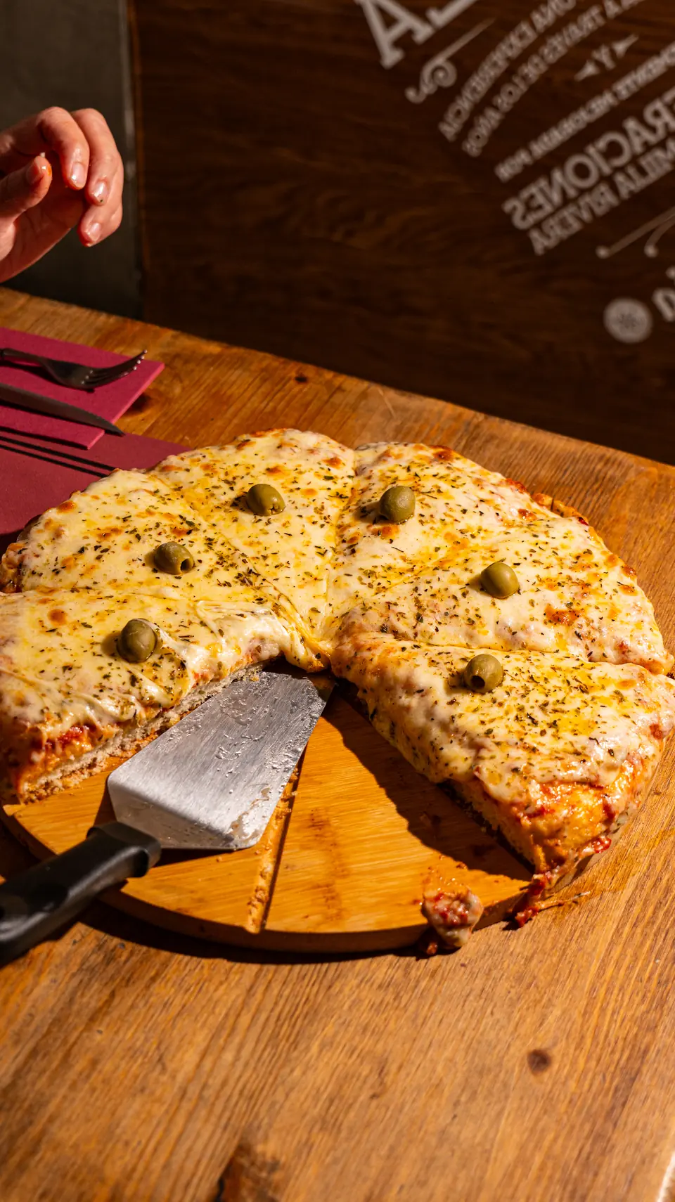 Pizza argentina de mitja massa amb mozzarella i olives, tallada sobre la taula de fusta
